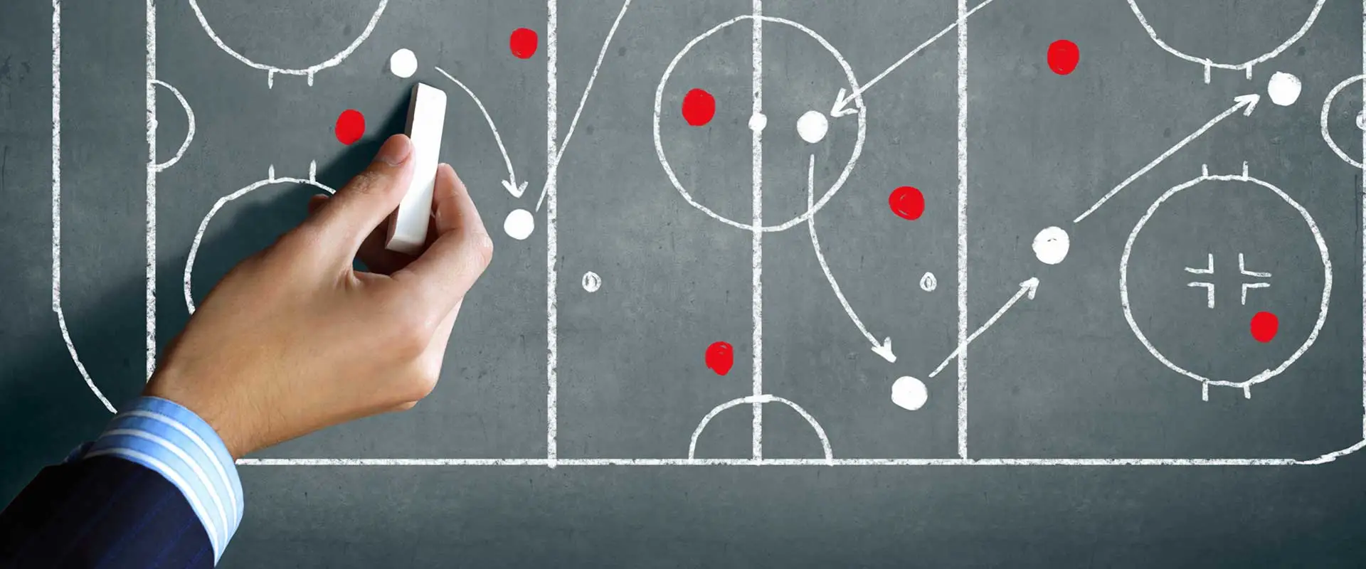hand with chalk plotting out a sports strategy on a chalk board