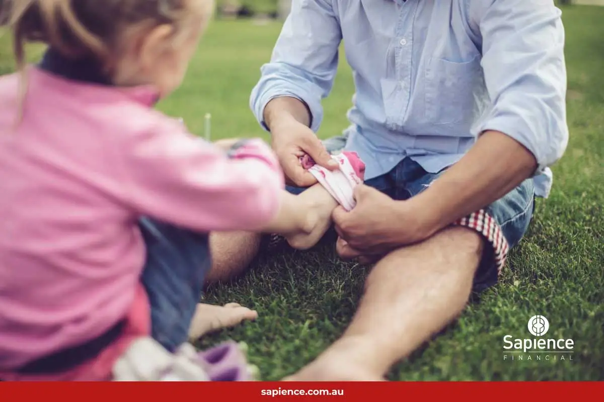 father putting sock on young child sitting on grass