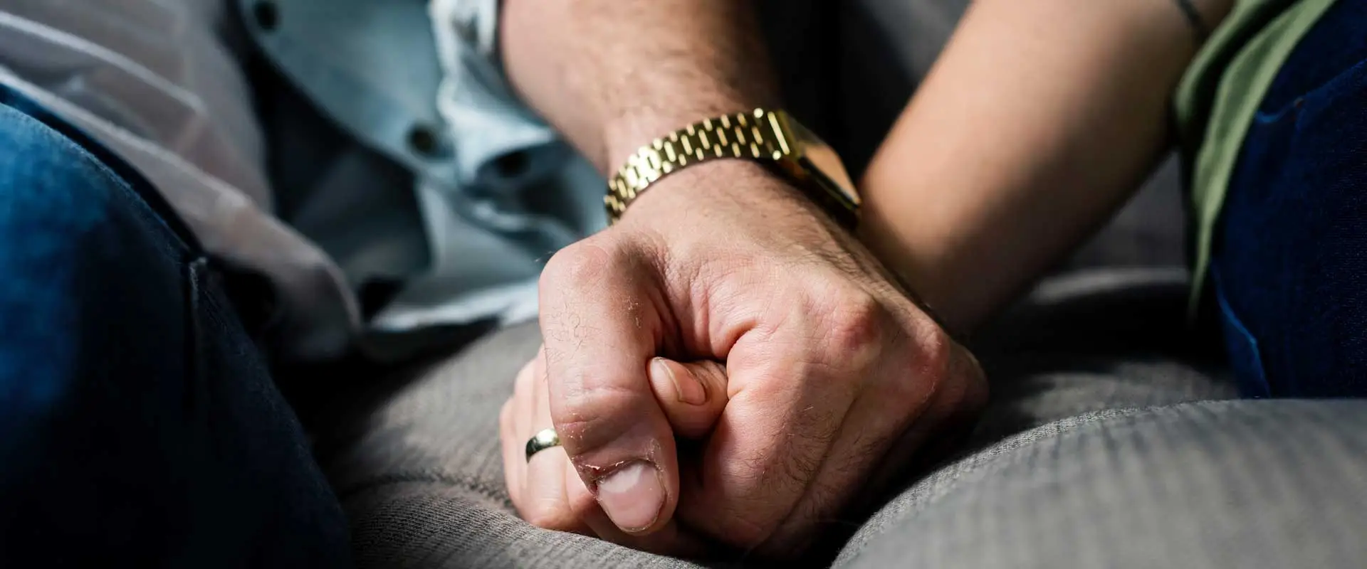 arms of a couple sitting on couch and holding each others hands