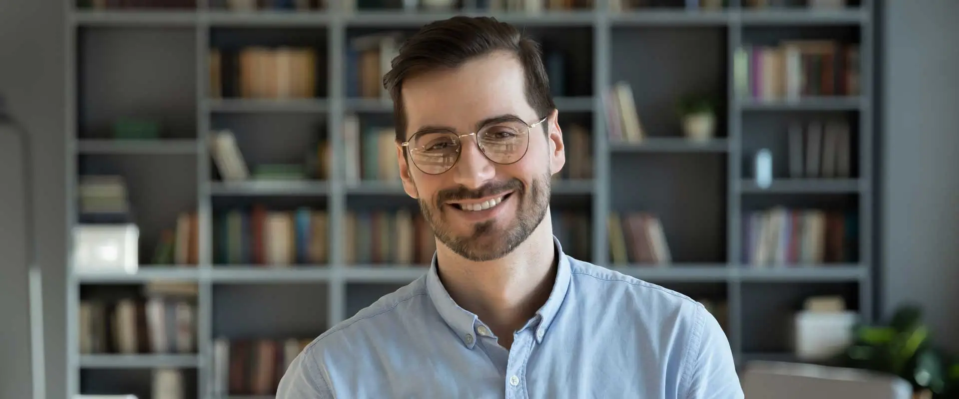 middle aged man wearing glasses and smiling while standing in front of a book shelf
